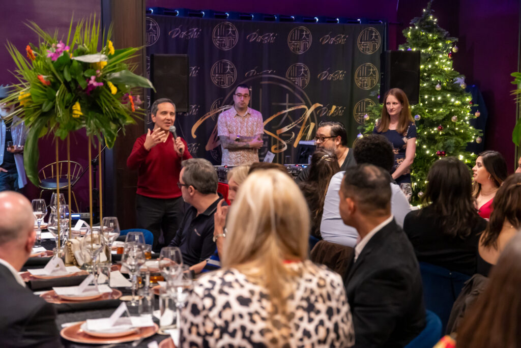 Man speaking with a microphone in front of people at a crowded restaurant